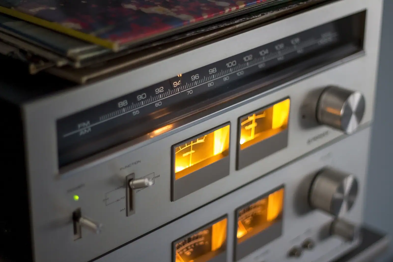 Ampli-tuner vintage au cadran FM éclairé et vu-mètres allumés, pochettes de disques posées derrière