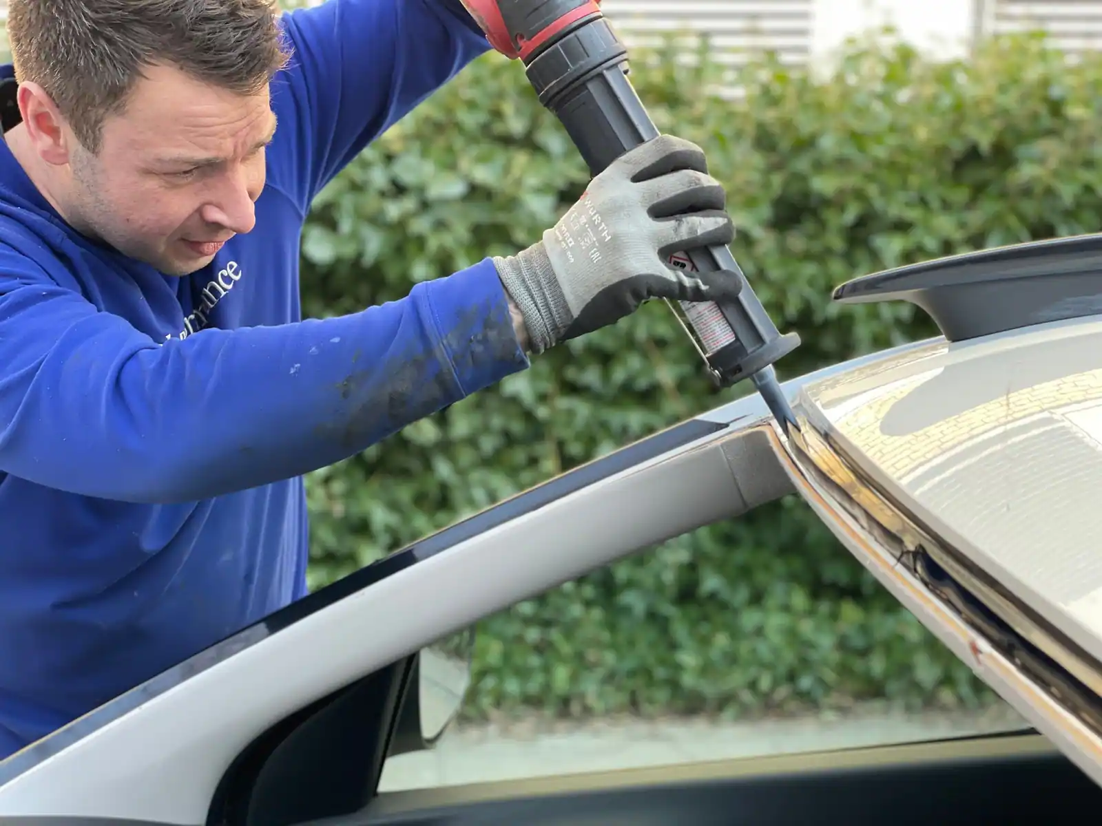 Technicien appliquant un cordon de colle sur le pourtour d'un pare-brise lors d'un remplacement.