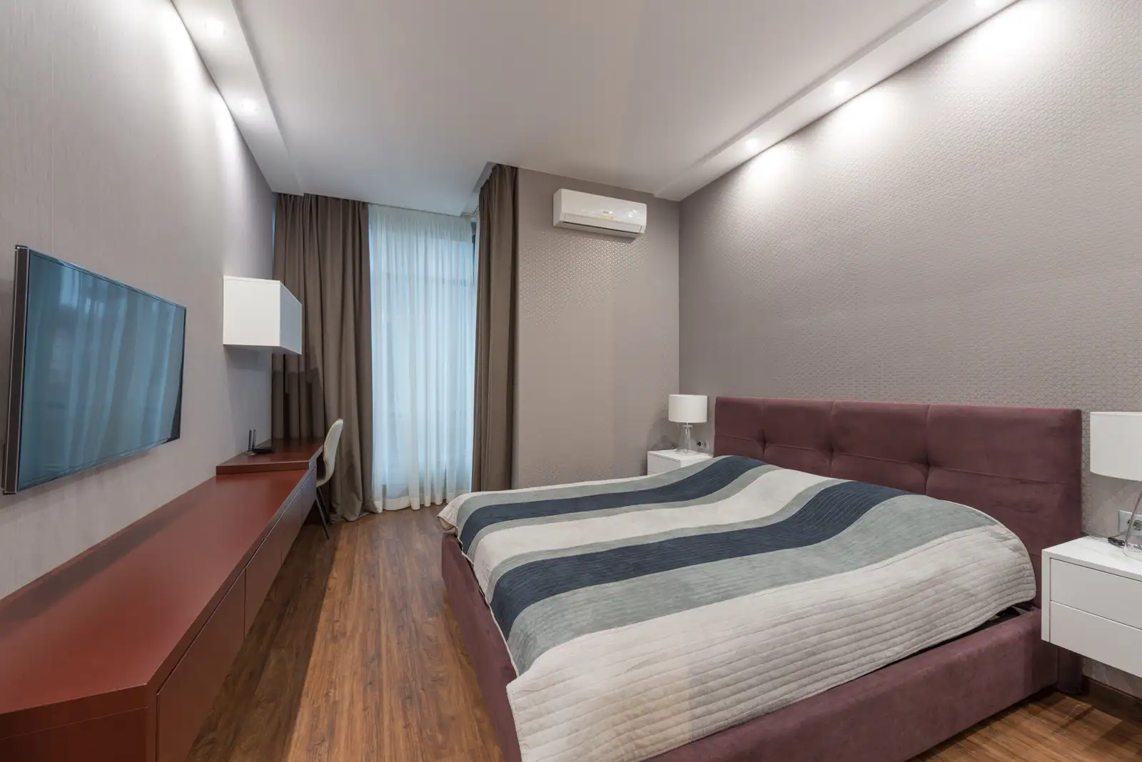 Chambre d’hôtel fonctionnelle avec lit double, bureau, téléviseur mural et rideaux tirés