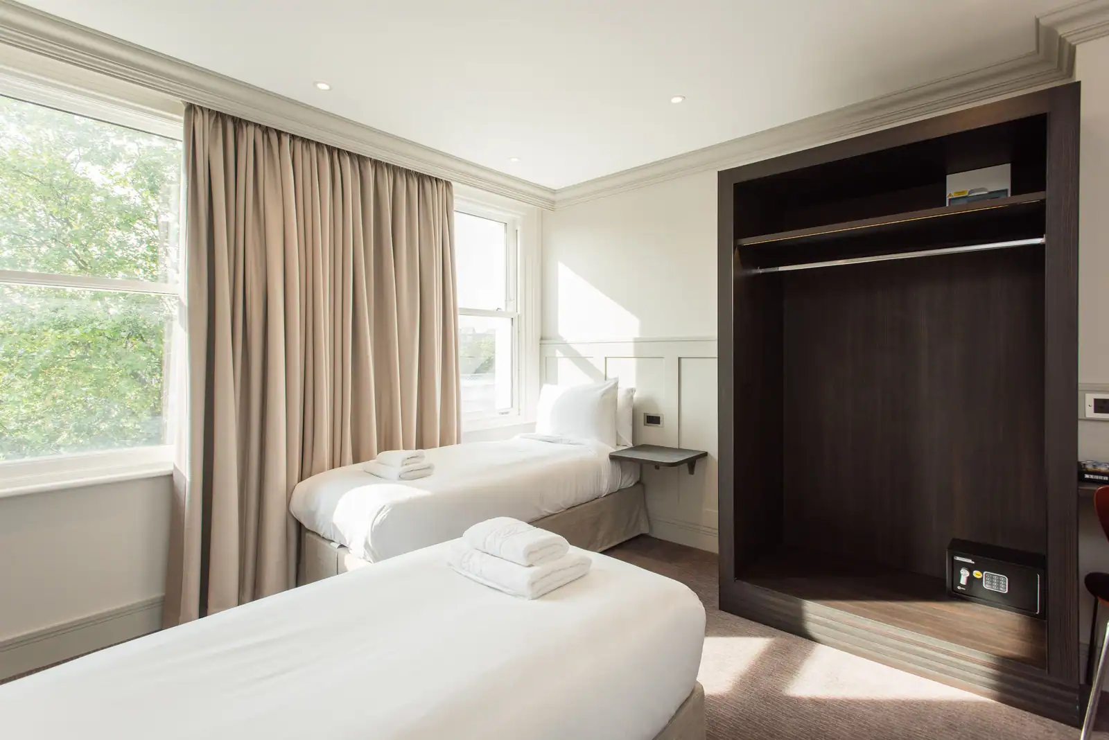 Chambre d'hôtel économique à deux lits simples, avec penderie intégrée et fenêtre donnant sur les arbres.