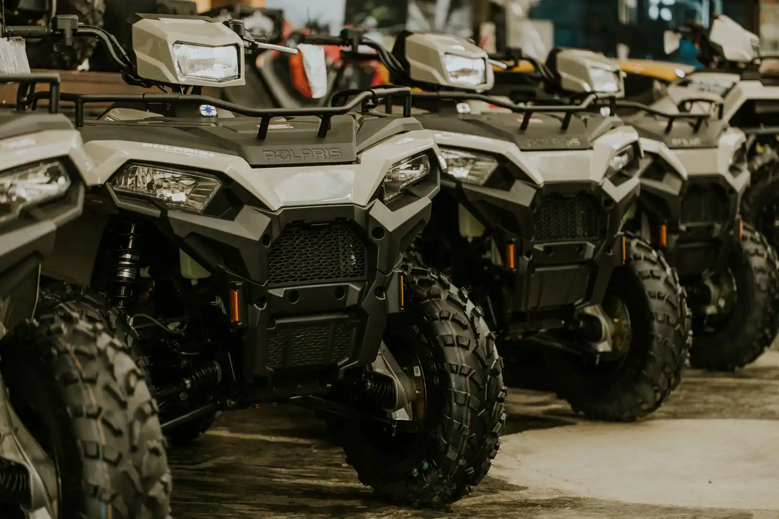 Rangée de quads neufs identiques alignés dans un hall, phares et pneus crantés au premier plan.