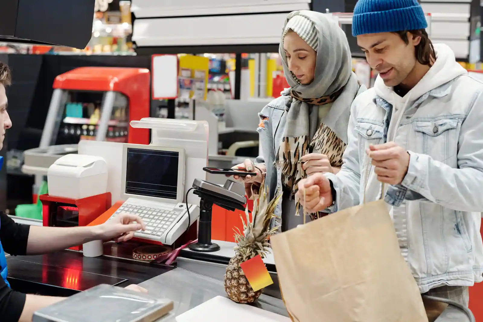 Cliente réglant ses courses avec son téléphone à la caisse d'un supermarché, devant le terminal de paiement