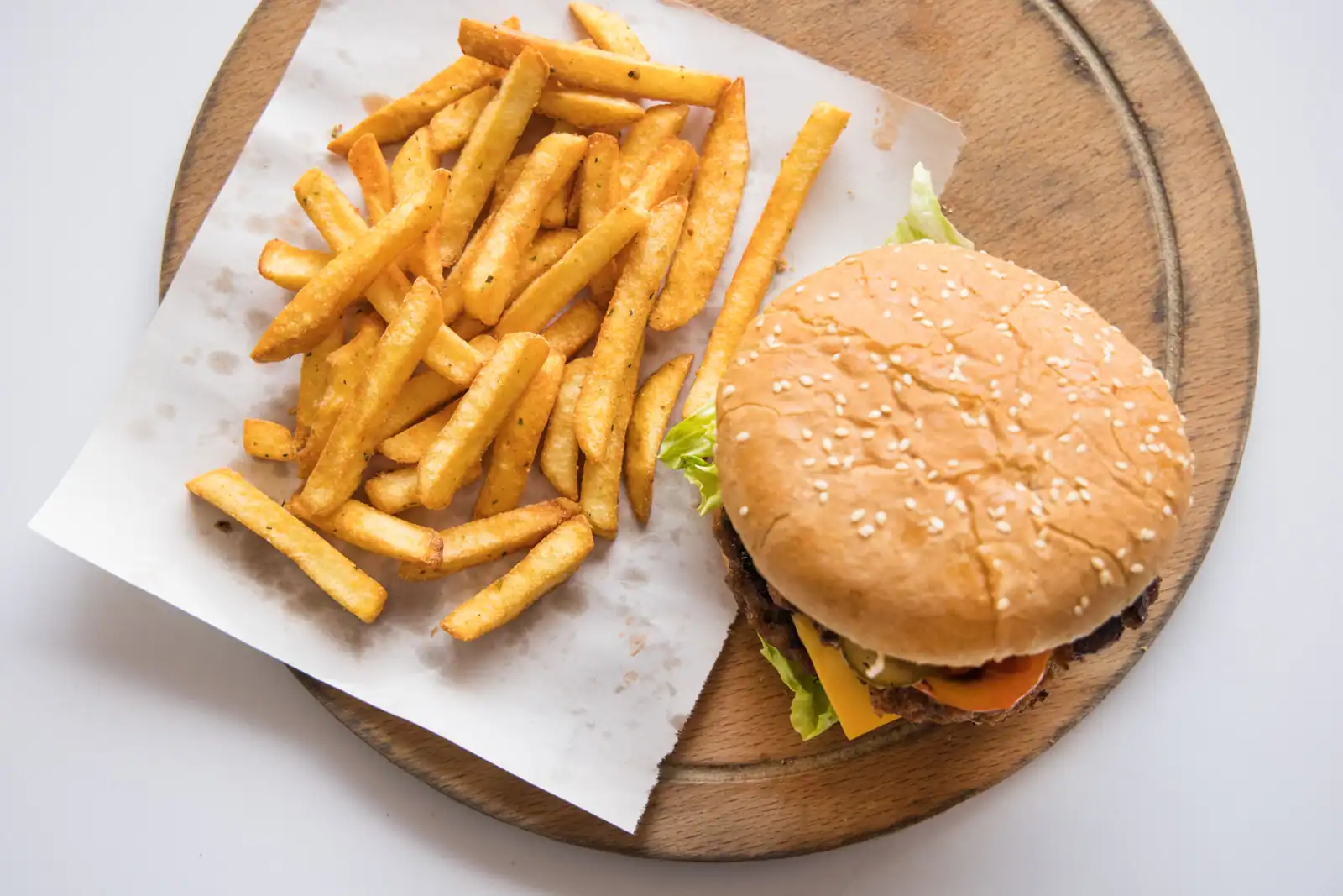 Un cheeseburger au pain aux graines de sésame et des frites, servis sur une planche en bois.
