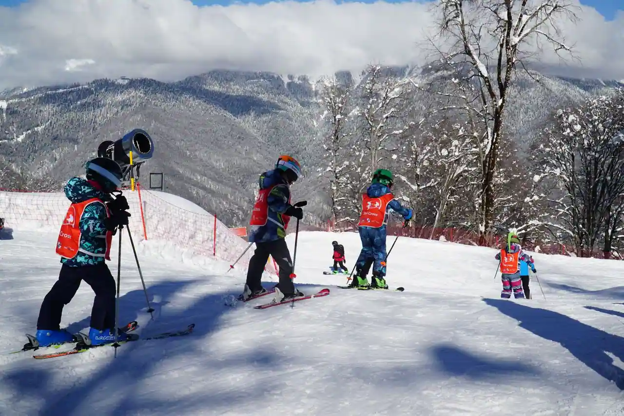 Groupe d’enfants casqués en chasubles de cours de ski, sur une pente douce enneigée face aux montagnes