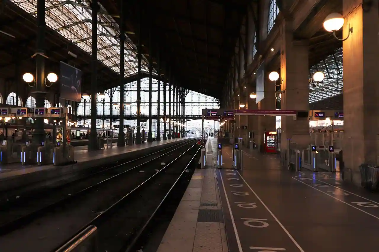Voies et quais déserts sous la verrière d’une grande gare parisienne, portiques d’accès allumés