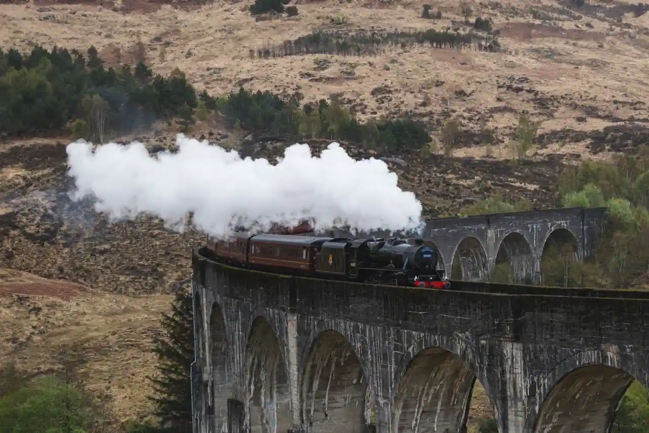 Train à vapeur franchissant un viaduc de pierre aux arches courbes, dans les Highlands écossaises.