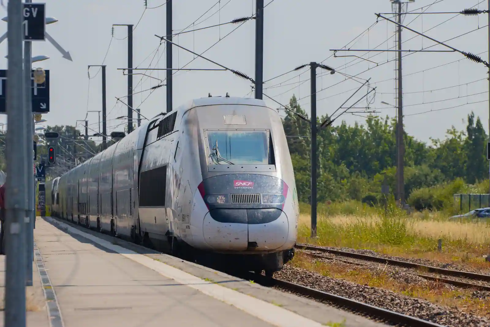 Rame TGV à l'approche du quai d'une gare française, sous les caténaires en plein soleil