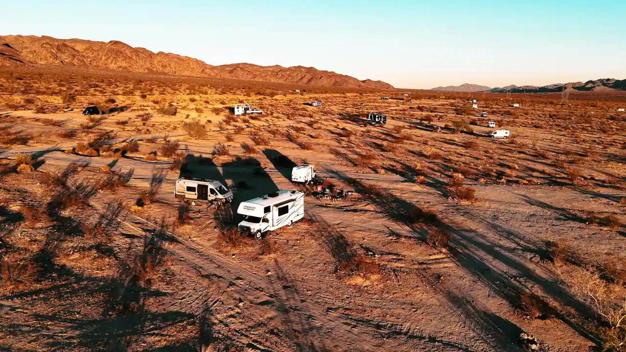 Plusieurs camping-cars regroupés pour la nuit sur un terrain désertique, au soleil couchant.
