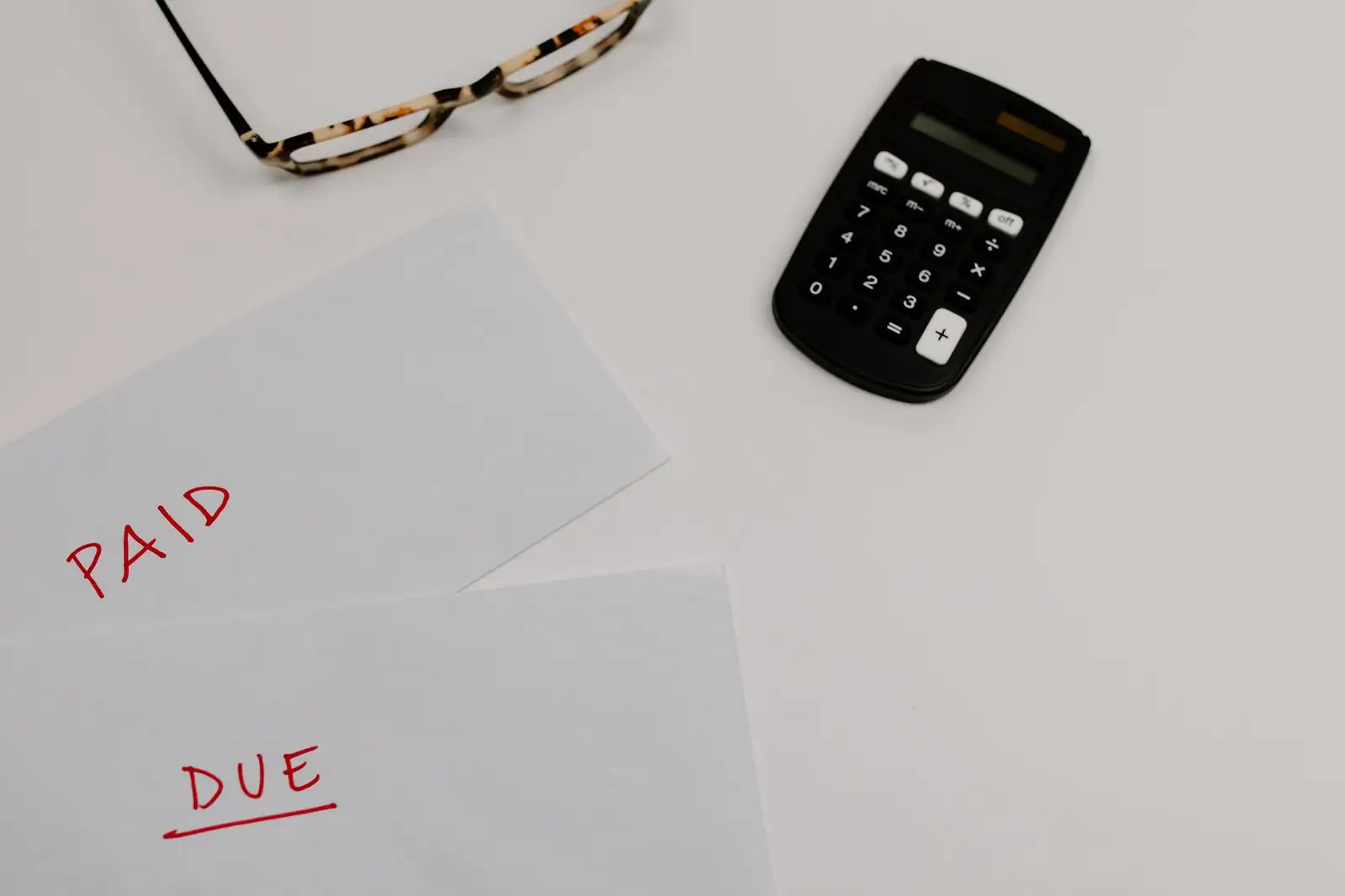 Papiers marqués « payé » et « à payer », posés près d'une calculette et de lunettes sur une table.