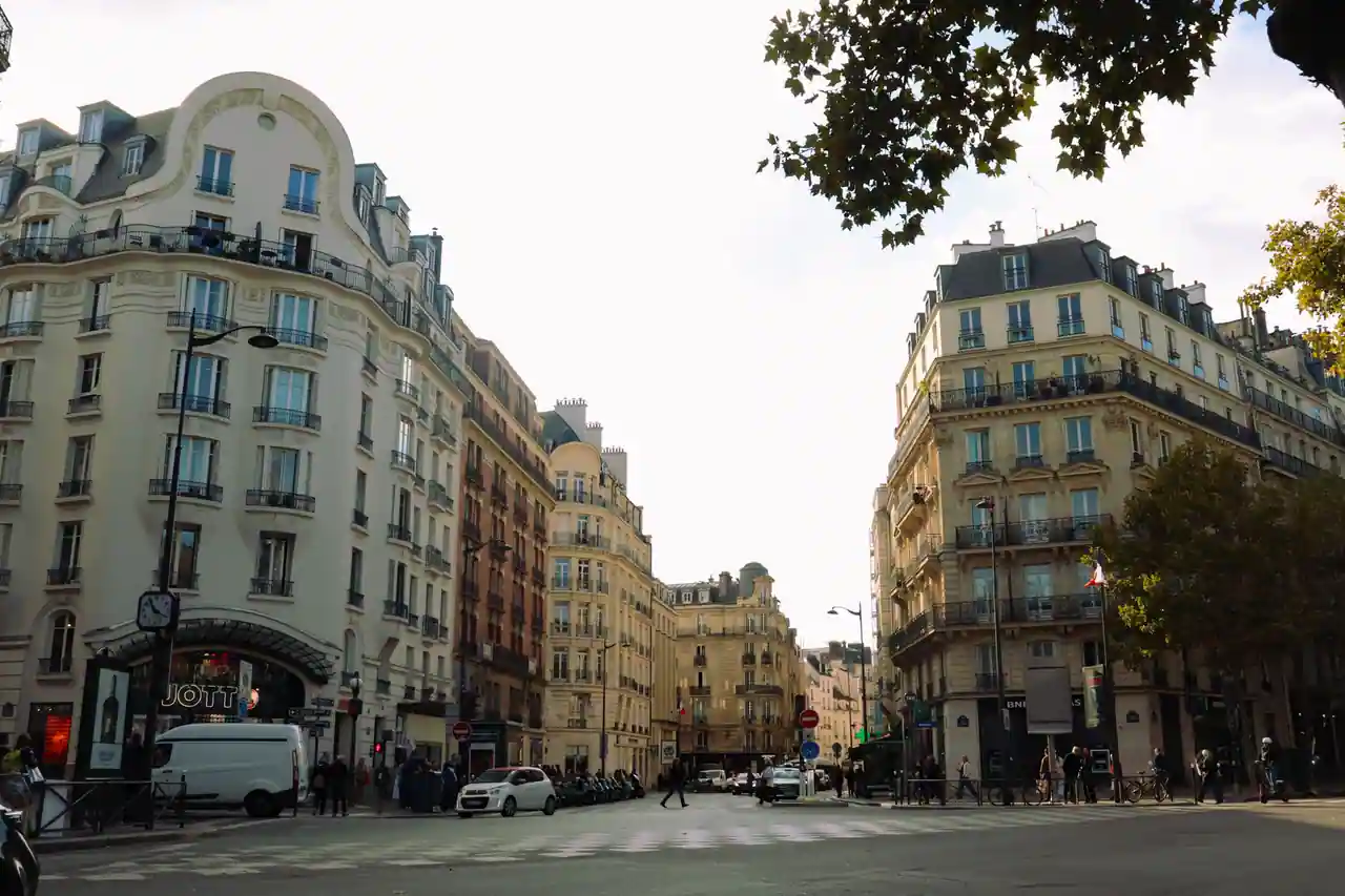 Carrefour parisien typique avec immeubles haussmanniens, balcons en fer forgé et vie de rue